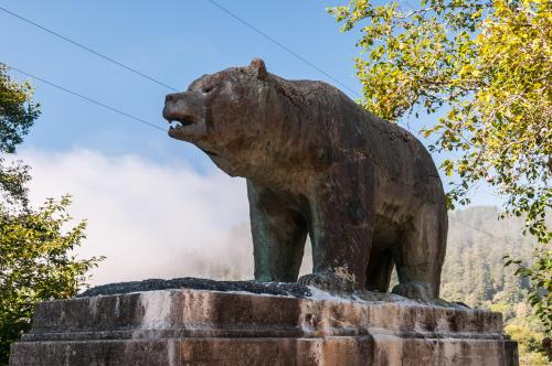 A large bronze bear statue stands on a stone pedestal, surrounded by trees and misty mountains in the background.