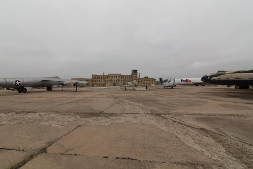 Abandoned airfield with vintage aircraft and a large building in the background under a cloudy sky.