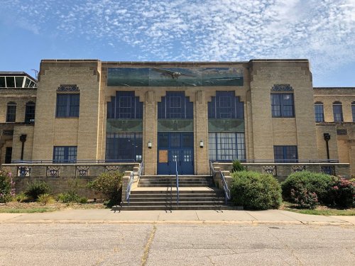 Historic brick building with large windows, decorative murals, and a staircase leading to the entrance, under a blue sky.
