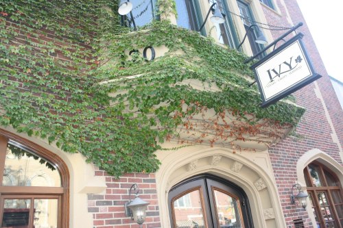 A brick building facade covered in green ivy, featuring a sign that reads "IVY" and decorative light fixtures.