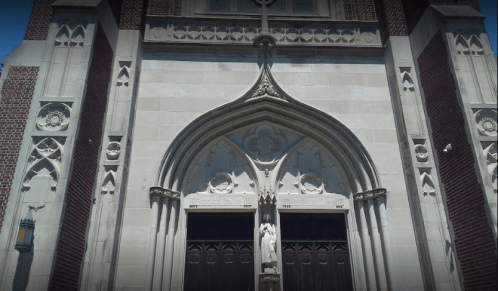 Gothic-style church entrance with ornate stonework and a central statue above the double doors.