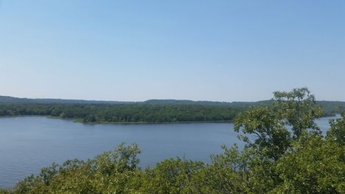 A serene view of a river winding through lush green trees under a clear blue sky.