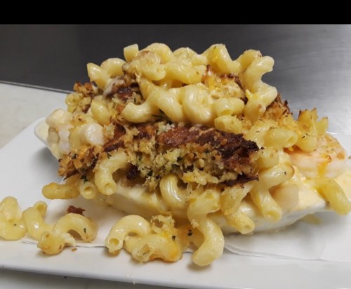 A plate of baked macaroni and cheese topped with crispy breadcrumbs, overflowing with pasta.