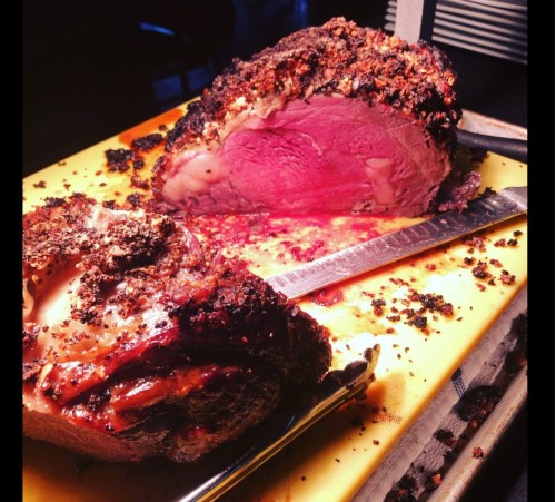 A perfectly cooked roast with a crispy crust, sliced to reveal juicy, pink meat inside, on a yellow cutting board.