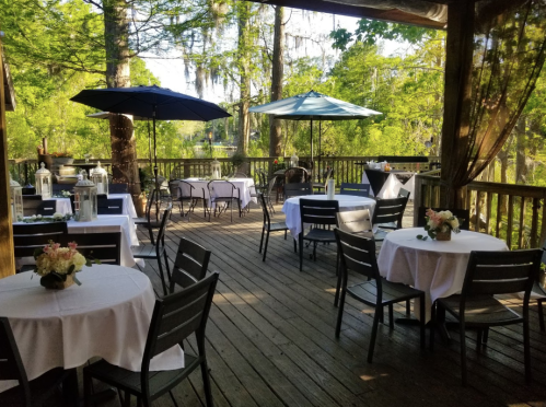 Outdoor dining area with white tablecloths, umbrellas, and lush greenery in the background.