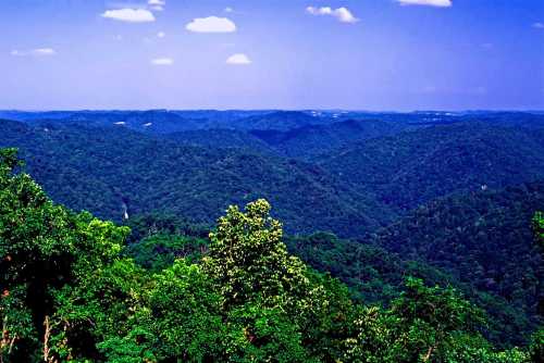 A panoramic view of lush green mountains under a blue sky with scattered clouds.