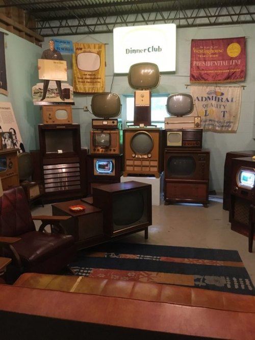 A retro display of vintage televisions and furniture in a cozy room, with colorful banners on the walls.