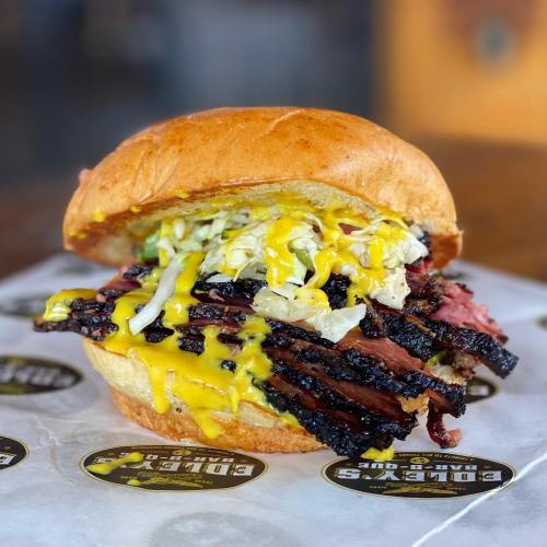 A close-up of a juicy brisket sandwich topped with mustard and shredded lettuce on a soft bun.