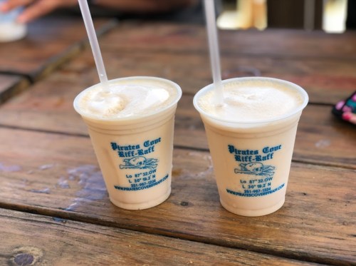 Two frosty drinks in clear cups with straws, sitting on a wooden table, featuring a logo for "Pirates Cove Riff-Raff."