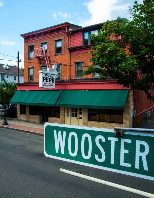 A brick building with a green awning and a sign for Frank Pepe Pizzeria, next to a street sign for Wooster.