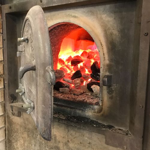 A close-up of an open furnace door, revealing glowing coals and flames inside.
