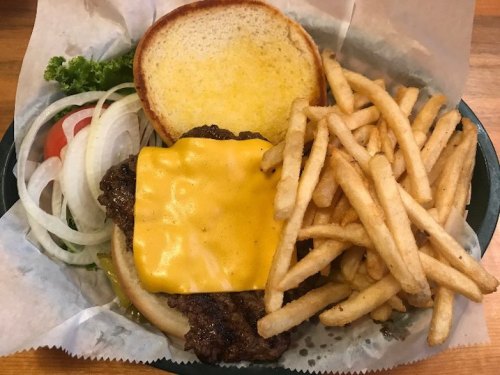 A cheeseburger with lettuce, tomato, and onion, served with a side of crispy fries in a basket.
