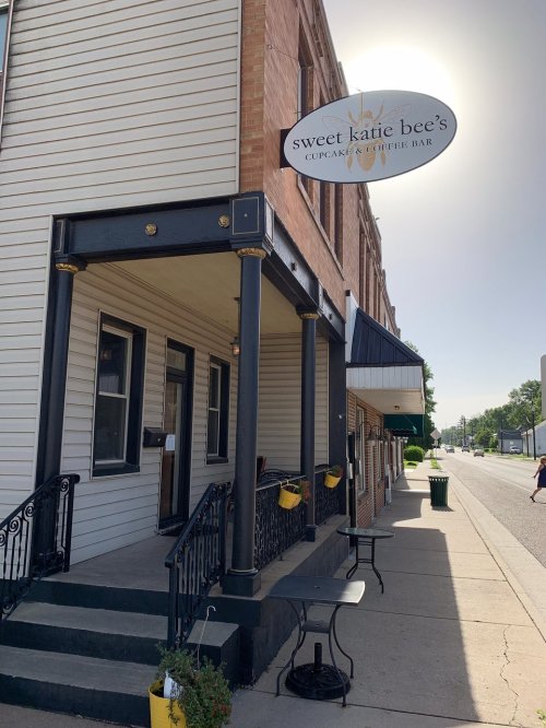 Exterior of Sweet Katie Bee's, a cupcake and coffee bar, featuring a sign and a small seating area on the porch.