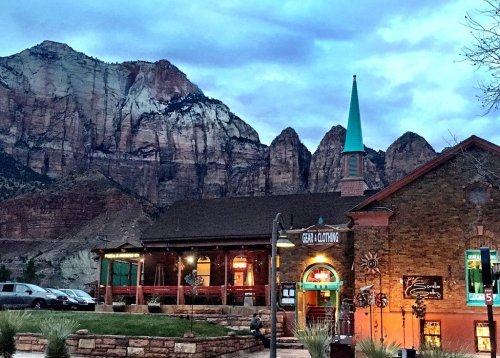 A rustic building with a green spire, set against dramatic mountains under a cloudy sky.