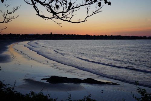 A serene beach at sunset, with gentle waves lapping the shore and a colorful sky reflected on the water.