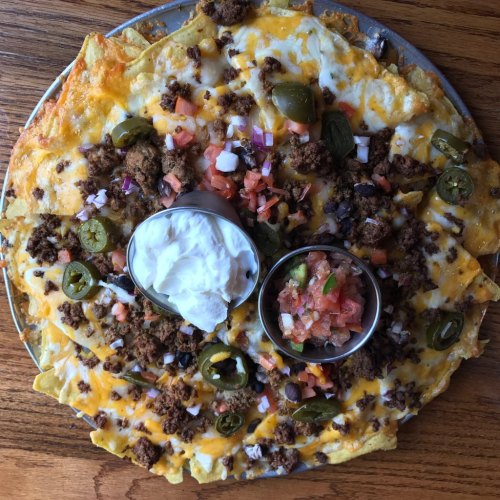 A large plate of nachos topped with cheese, ground beef, jalapeños, tomatoes, onions, and served with sour cream and salsa.