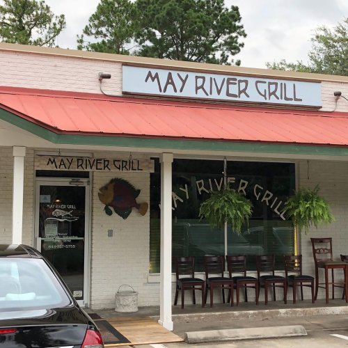 Exterior of May River Grill featuring a sign, potted ferns, and empty chairs outside the restaurant.