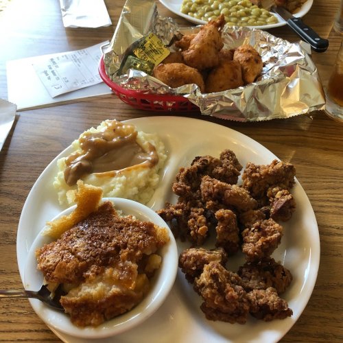 A plate of fried chicken, mashed potatoes with gravy, cornbread, and a side of fried snacks on a wooden table.