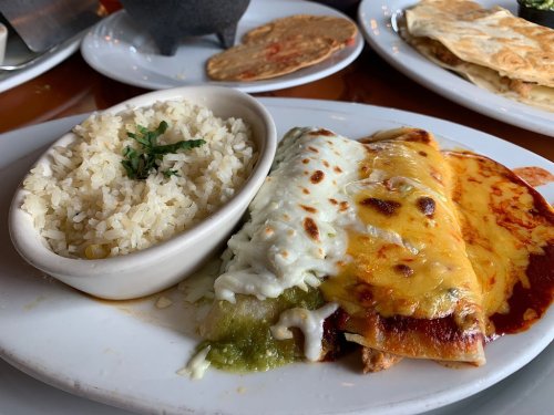 A plate of enchiladas topped with red and green sauces, served with a side of rice and garnished with herbs.