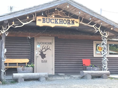 A rustic wooden building with a sign reading "Buckhorn" and antler decorations, featuring a bar entrance and outdoor seating.
