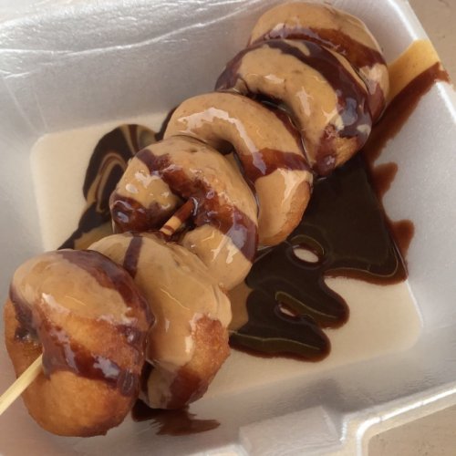 A skewer of four doughnut holes drizzled with chocolate and peanut butter sauce, served in a takeout container.