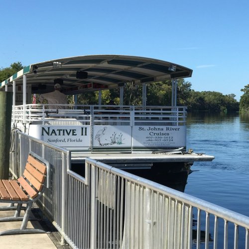 A boat named "Native II" docked at St. Johns River in Sanford, Florida, with clear blue skies and calm water.