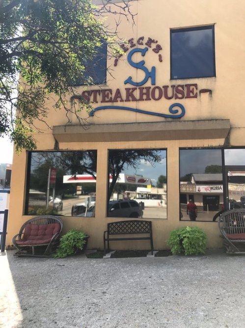 Exterior of a steakhouse with large windows, a sign reading "Steech's Steakhouse," and outdoor seating.