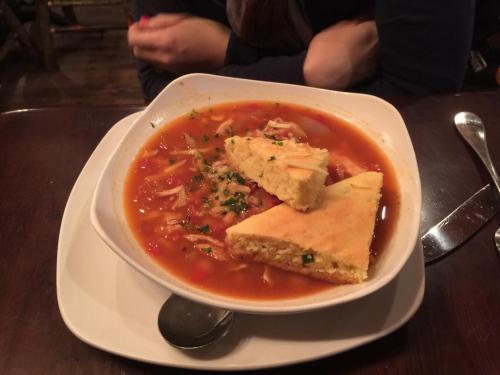 A bowl of soup with vegetables and chicken, served with two pieces of cornbread on the side.