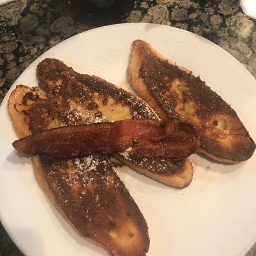 A plate with two pieces of French toast topped with chocolate spread and a strip of crispy bacon.