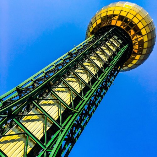 A tall green tower with a golden observation dome against a clear blue sky.