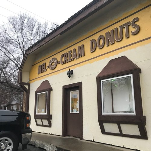 Exterior of Mel Cream Donuts shop with a yellow facade and brown accents, featuring a "OPEN" sign in the window.