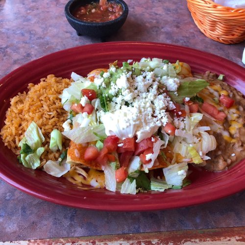A vibrant plate of enchiladas topped with lettuce, tomatoes, cheese, and sour cream, served with rice and beans.