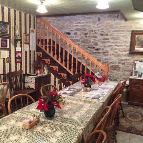 Cozy dining area with wooden chairs, a lace tablecloth, and festive decorations, featuring a staircase in the background.