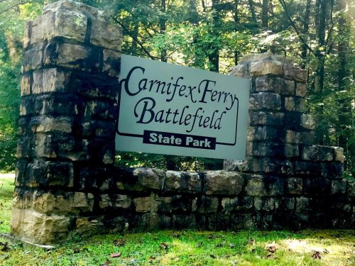 Sign for Carnifex Ferry Battlefield State Park, framed by stone, surrounded by trees in a natural setting.