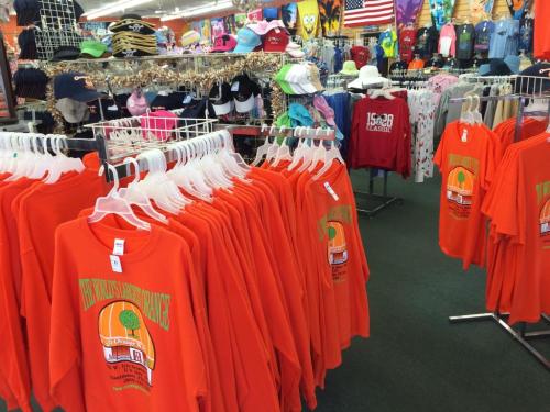 A retail store display featuring colorful clothing, including orange t-shirts and various hats on racks.