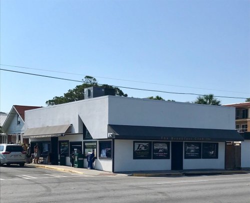 A small, white building with a sign reading "The Breakfast Club" and outdoor seating on a sunny day.