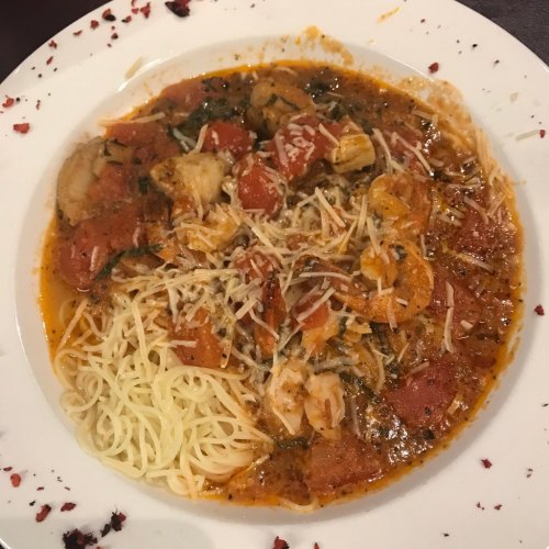 A plate of pasta with shrimp, tomatoes, and herbs, topped with grated cheese, served in a rich sauce.