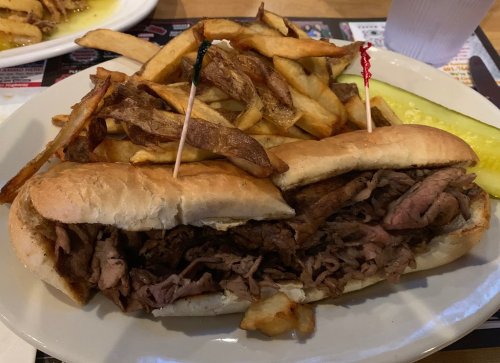 A hearty sandwich filled with sliced roast beef, served with crispy fries and a pickle on the side.