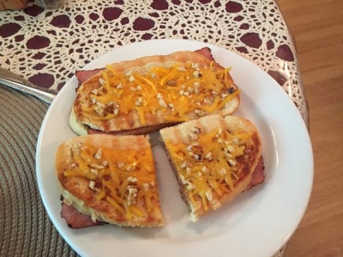 A plate with three pieces of toasted bread topped with ham, melted cheese, and chopped nuts.