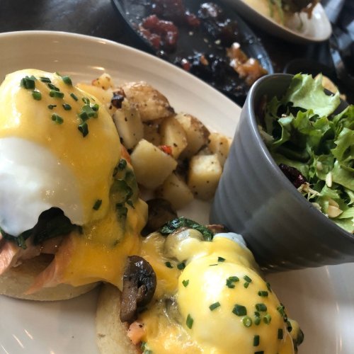 A plate of eggs Benedict with spinach and cheese, served with roasted potatoes and a side salad.