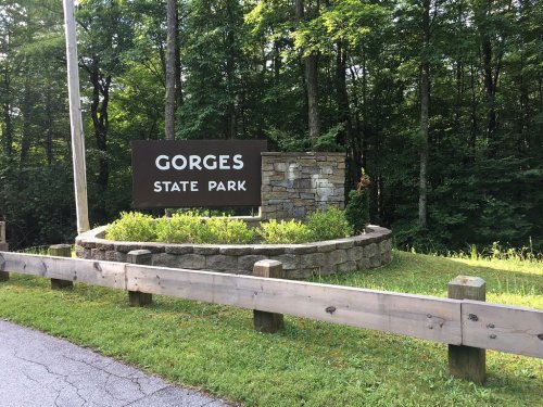 Sign for Gorges State Park surrounded by greenery and a wooden fence.