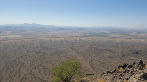A panoramic view of a vast desert landscape with mountains in the distance and a clear blue sky.