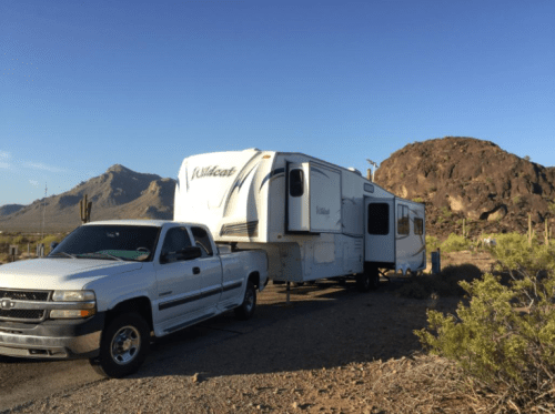 A white pickup truck parked next to a large RV in a desert landscape with mountains in the background.