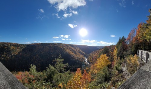 A panoramic view of a colorful autumn landscape with a river winding through the valley under a bright sun.