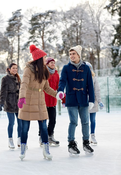 A group of friends ice skating outdoors, smiling and enjoying the winter scenery.