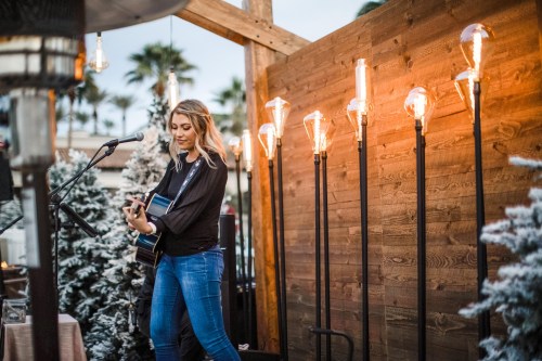 A woman plays guitar on stage, surrounded by festive decor and glowing light fixtures.