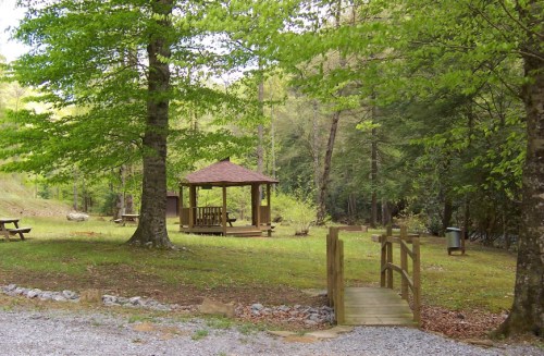 A peaceful park scene featuring a gazebo, wooden bridge, and lush green trees.