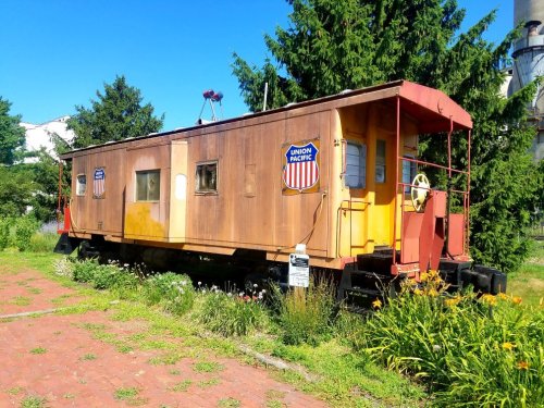 A vintage Union Pacific caboose on display, surrounded by greenery and flowers under a clear blue sky.