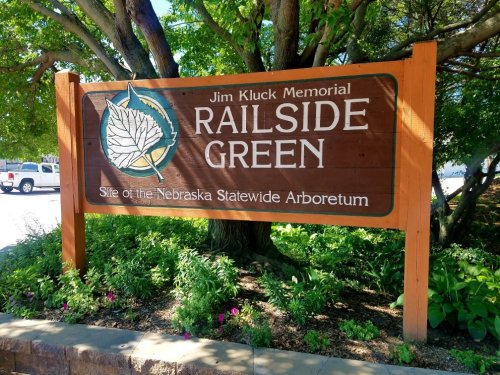 Sign for Jim Kluck Memorial Railside Green, home of the Nebraska Statewide Arboretum, surrounded by greenery.