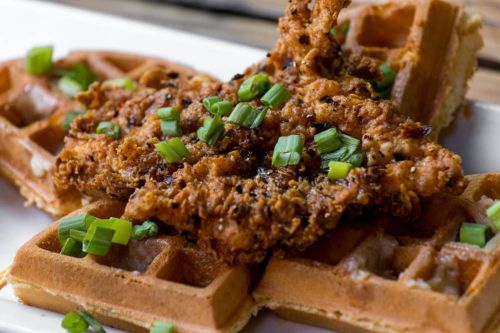 A plate of crispy fried chicken atop golden waffles, garnished with chopped green onions.
